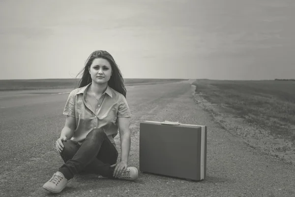 Girl siting on road with suitcase looks for fellow traveler — Stock Photo, Image