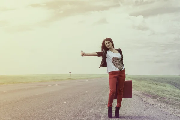 Girl standing on road with suitcase looks for fellow traveler — Stock Photo, Image