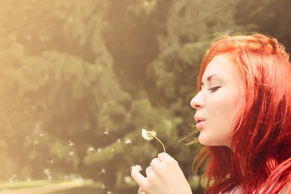 Beautiful woman with red hair blows into dandelion — Stock Photo, Image