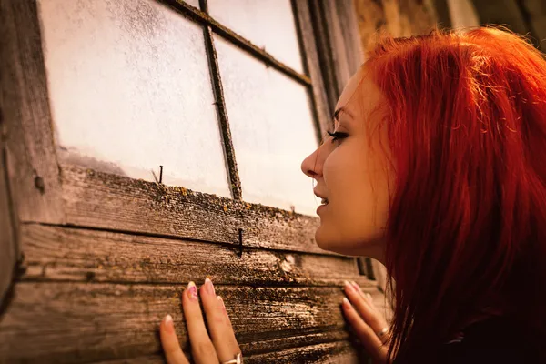 Woman curiously looks in window of old house — Stock Photo, Image