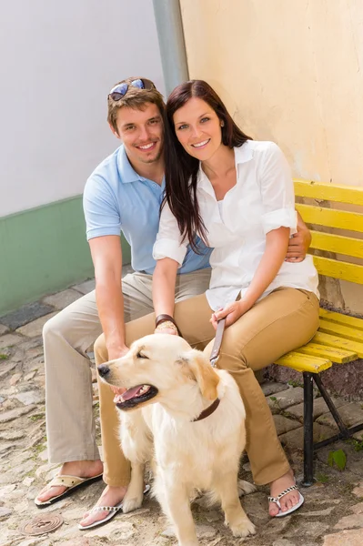 Šťastný pár se psem sedí žlutý lavička — Stock fotografie