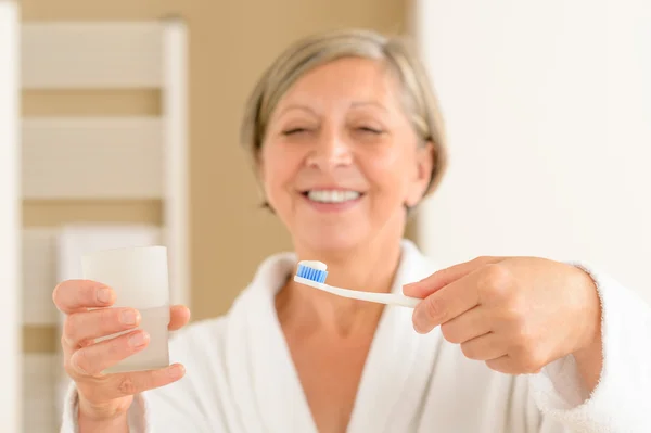 Donna anziana tenere spazzolino da denti e acqua di vetro — Foto Stock