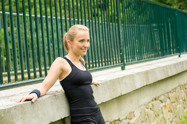 Sportive girl resting against fence after workout — Stock Photo, Image