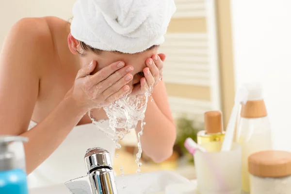 Frau spritzt im Badezimmer mit Wasser ins Gesicht Stockbild