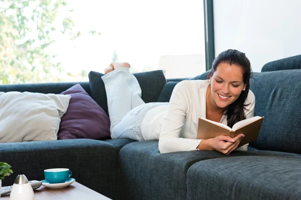 Ung kvinna liggande läsande bok soffa soffa — Stockfoto