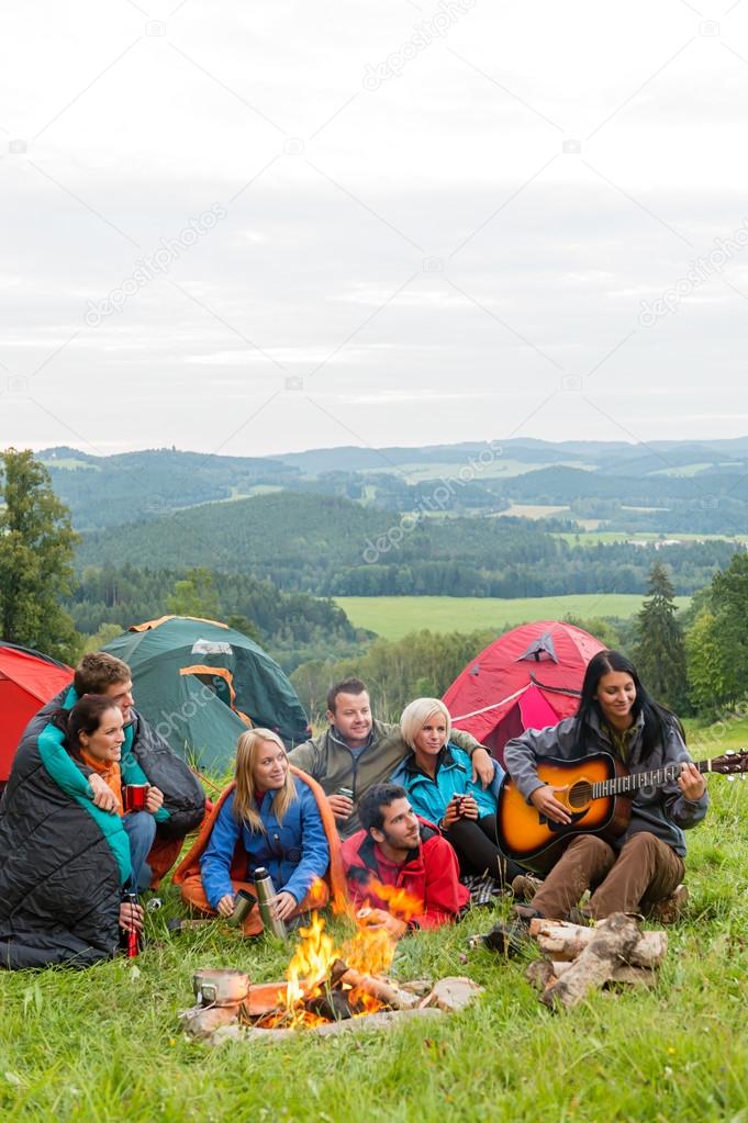 Camping friends playing guitar beside fire nature