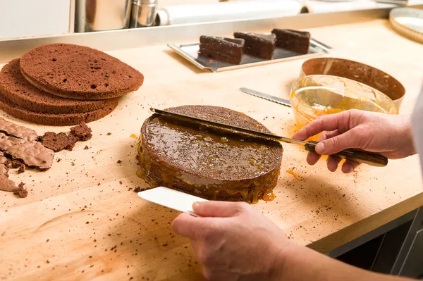 Cozinhe espalhando molho no bolo na cozinha — Fotografia de Stock