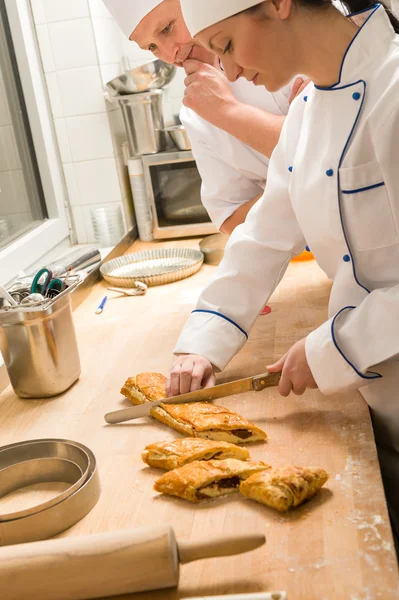 Female baker slicing strudel with male cook — Zdjęcie stockowe