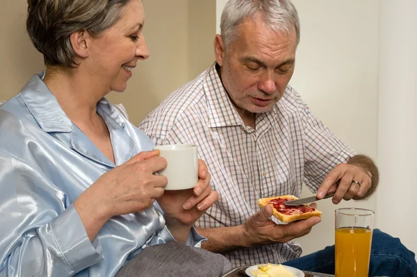 वृद्ध जोडपे बेडमध्ये रोमँटिक नाश्ता खाणे स्टॉक फोटो