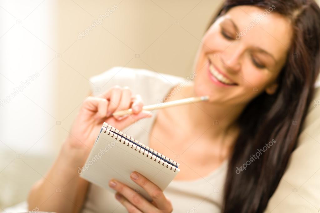 Pensive brunette woman writing to notebook