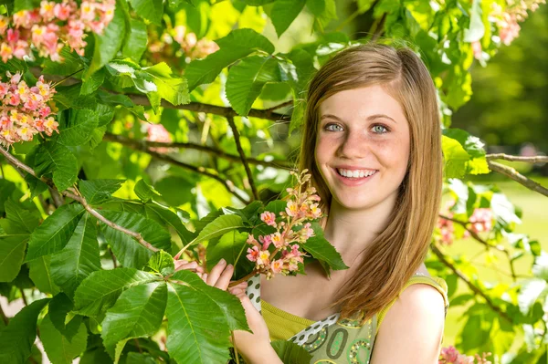 Young girl holding blossom in sunny park — Stock Photo, Image