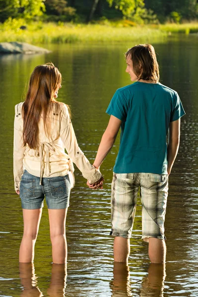 Teenage par stående i vatten som håller hand — Stockfoto