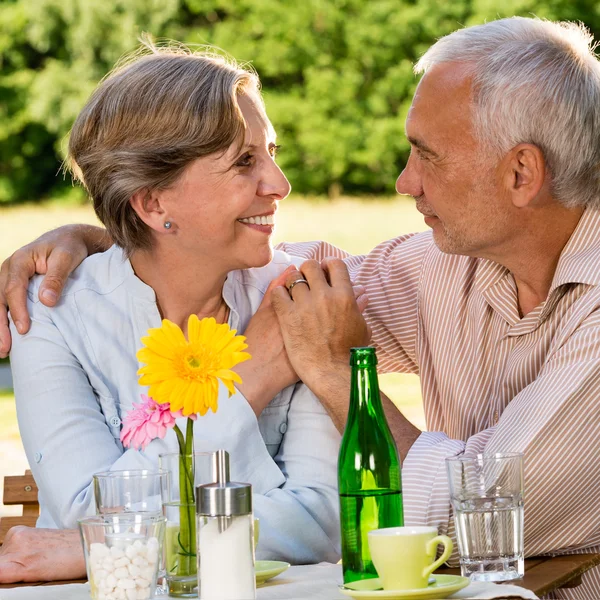 Gepensioneerde paar zitten aan tafel hand in hand — Stockfoto