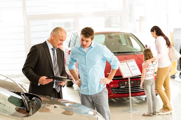 Car agent showing vehicle to young family — Stock Photo, Image