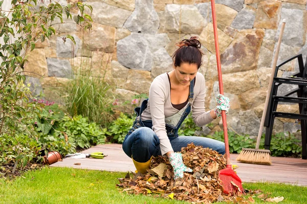 Jovem mulher raking folhas outono pilha varanda — Fotografia de Stock