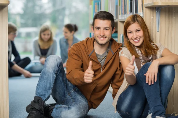 Estudiantes felices mostrando pulgar hacia arriba en la biblioteca —  Fotos de Stock