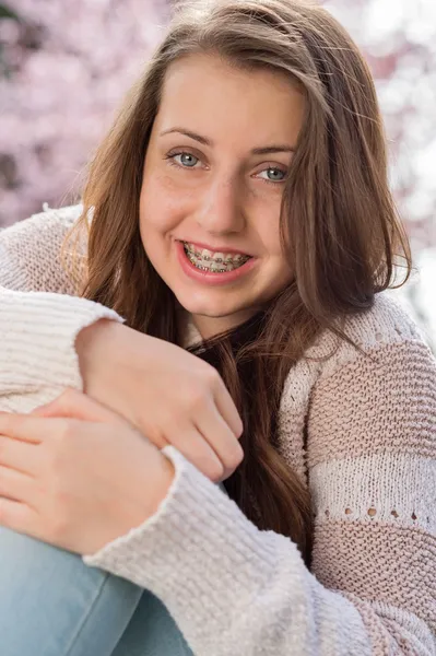 Girl with braces hugging knees in nature — Stock Photo, Image