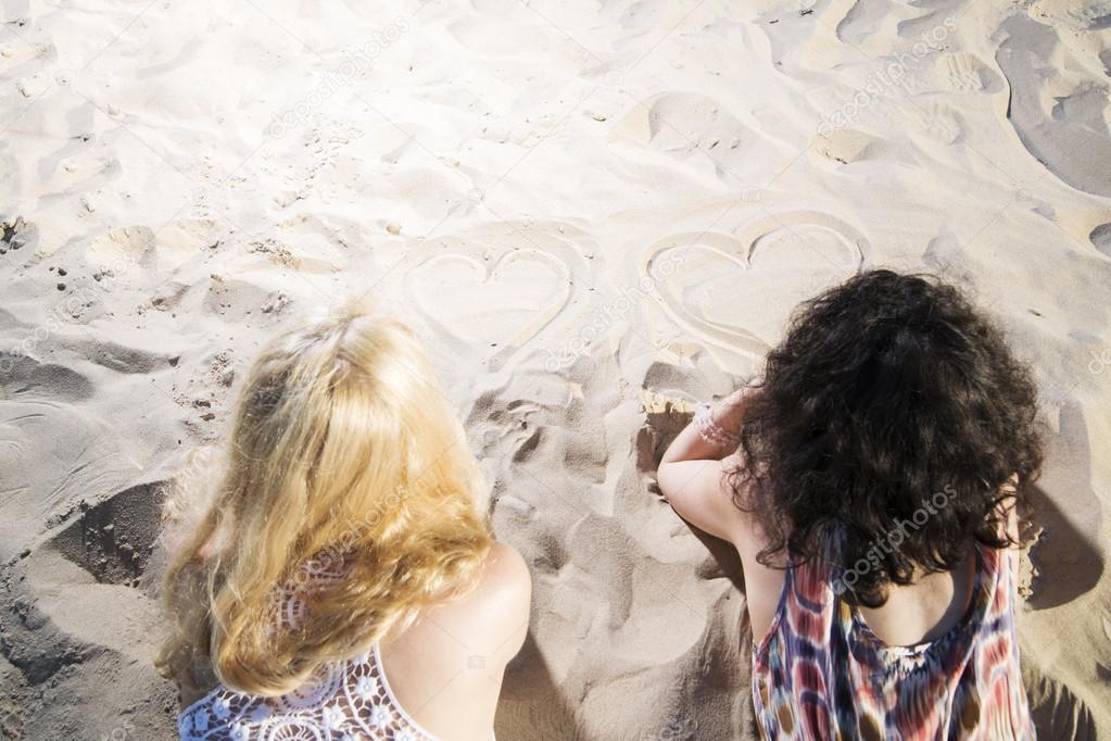 Two young womans draw hearts on sand.