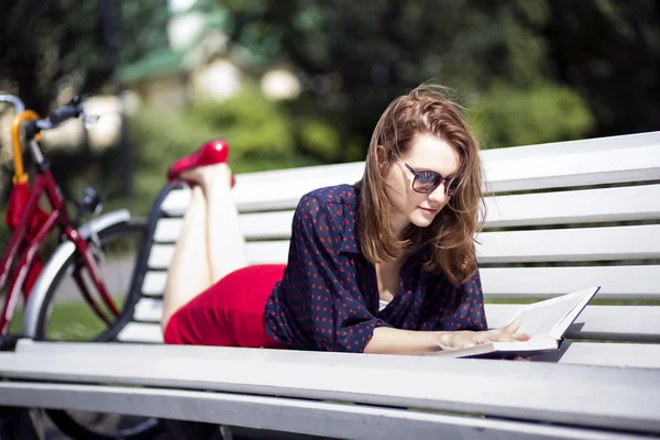 Kvinna liggande på bänken och läsa bok — Stockfoto