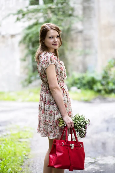 Donna in abito tenere fiori e borsa — Foto Stock