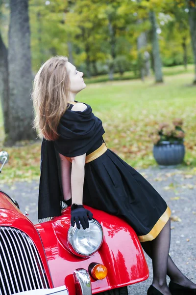 Woman in black posing on car headlight — Stock Photo, Image