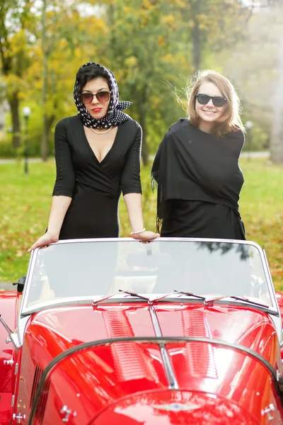 Les jeunes femmes en rouge rétro voiture sur la route — Photo