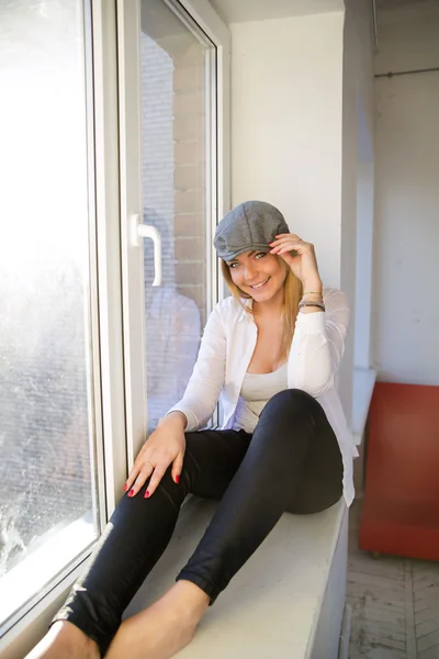 Kvinna på fönsterkarmen leende och beröring hatt — Stockfoto