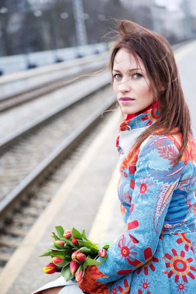 Mulher espera trem com flores à mão — Fotografia de Stock