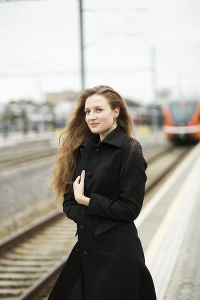 Mulher de casaco preto esperando trem laranja — Fotografia de Stock