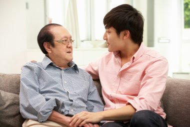 Portrait Of Chinese Father With Adult Son Relaxing At Home clipart