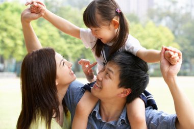 Chinese Family Giving Daughter Ride On Shoulders In Park clipart