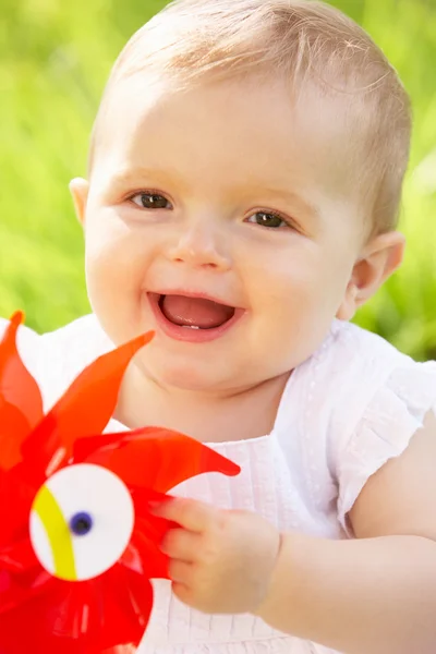 Baby flicka i sommarklänning sitter i fältet håller väderkvarn — Stockfoto