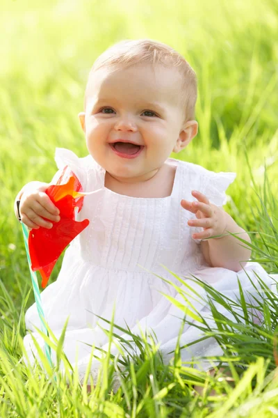 Bebé en vestido de verano sentado en campo sosteniendo molino de viento —  Fotos de Stock