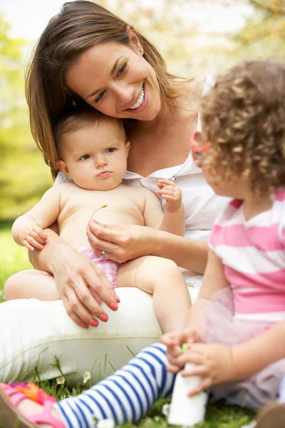 Mamma sitter med döttrar i fältet av sommarblommor — Stockfoto