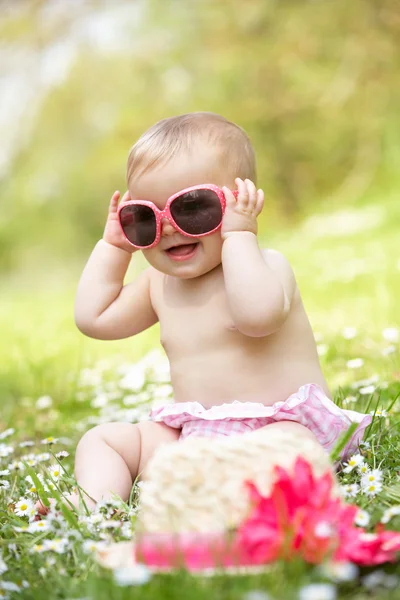 在字段中戴着墨镜坐在夏天穿裙子的宝宝女孩 — 图库照片