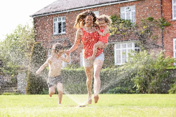 Mãe e duas crianças que correm através do aspersor do jardim — Fotografia de Stock