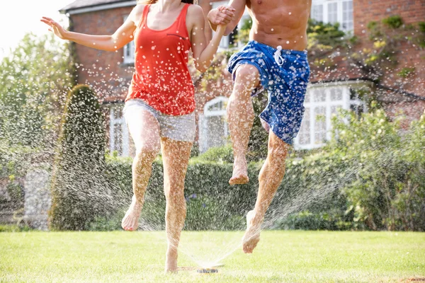 Paar läuft durch Gartensprenger — Stockfoto