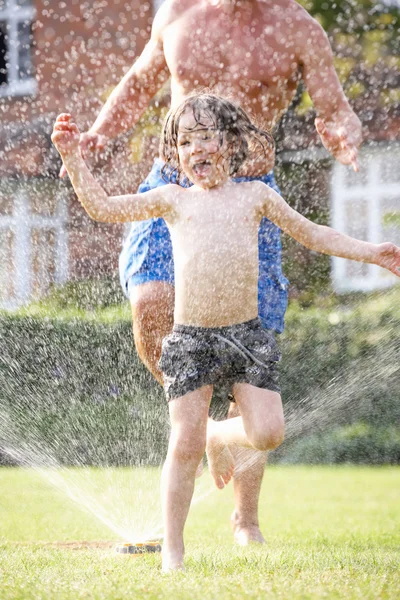 Far och son kör genom trädgården sprinkler — Stockfoto