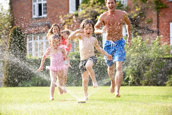 Familia corriendo a través de rociadores de jardín — Foto de Stock