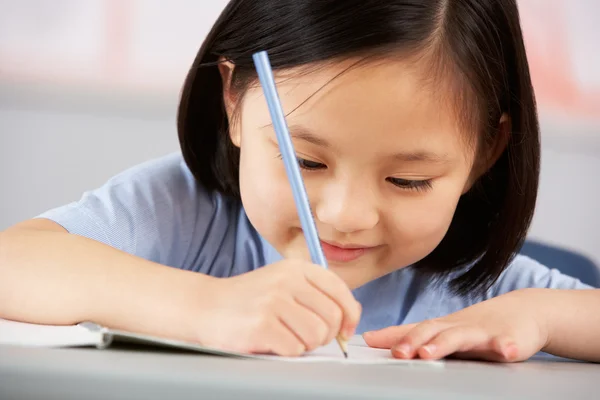 Kvinnlig student arbetar på skrivbord i kinesiska skola klassrum — Stockfoto