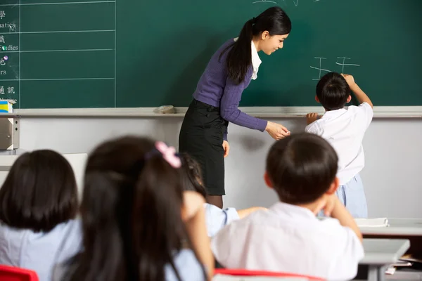 Alumno masculino escribiendo en pizarra en el aula de la escuela china — Foto de Stock