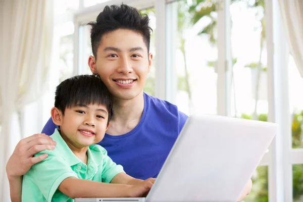 Pai e filho chineses sentados à mesa usando laptop em casa — Fotografia de Stock