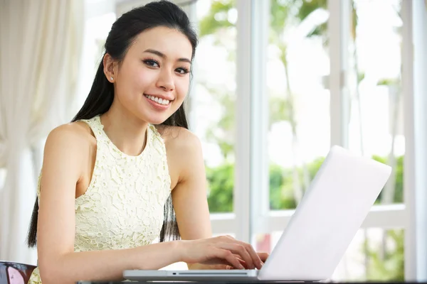 Joven mujer china sentada en el escritorio usando el ordenador portátil en casa —  Fotos de Stock