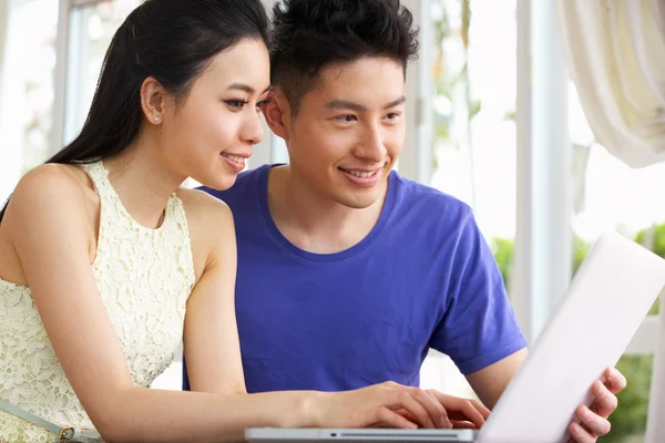 Joven pareja china sentada en el escritorio y usando el ordenador portátil en casa — Foto de Stock