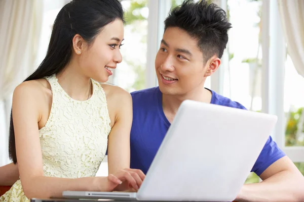 Casal chinês jovem sentado na mesa e usando laptop em casa — Fotografia de Stock