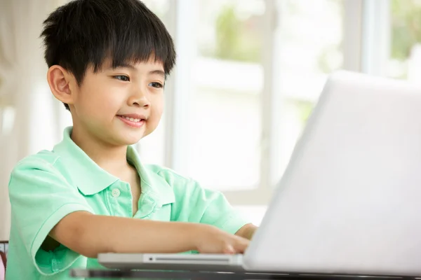 Молодой китайский мальчик сидит за столом с ноутбуком дома — стоковое фото