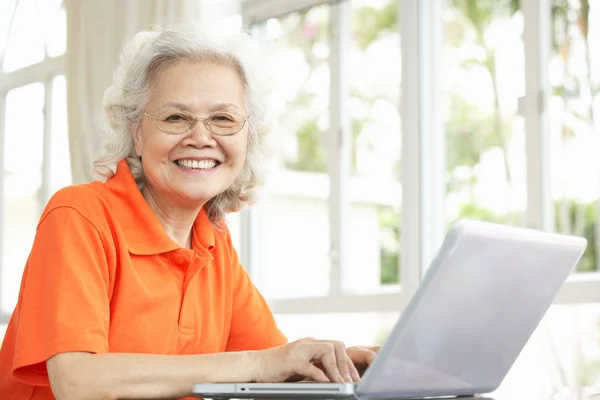 Senior chinese vrouw zit aan bureau met behulp van laptop thuis — Stockfoto
