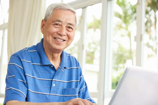 Starszy mężczyzna chiński siedząc przy biurku, za pomocą laptopa w domu — Zdjęcie stockowe