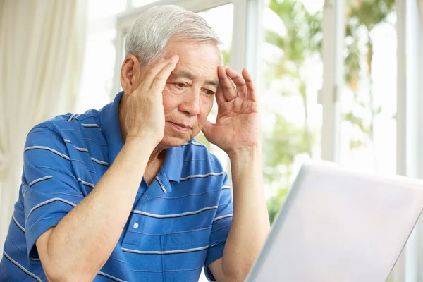 Martwi się starszy człowiek chiński siedząc przy biurku, za pomocą laptopa w domu — Zdjęcie stockowe