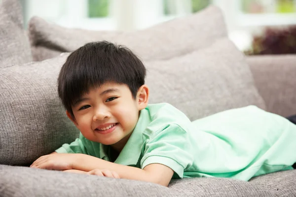 Menino chinês jovem relaxando no sofá em casa — Fotografia de Stock